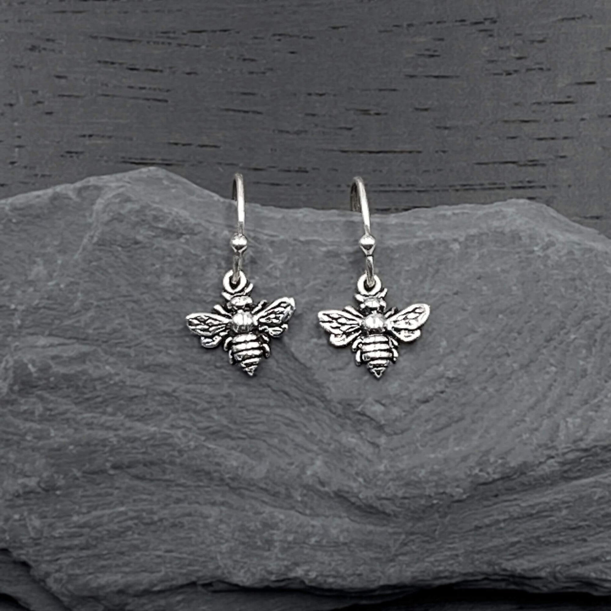 Detailed view of silver dangling earrings with a intricate bee design.