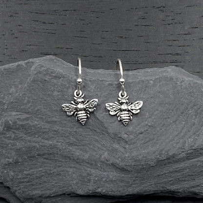 Detailed view of silver dangling earrings with a intricate bee design.