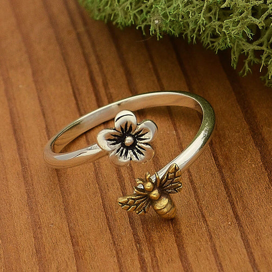 Close up of a sterling silver adjustable band ring with a sterling flower on one open end and a gold bronze bee on the other. 