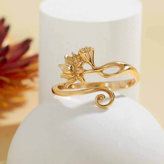 Close up of a shiny gold adjustable band ring with a lotus flower and louts bud on one side and a shiny gold swirl on the other. 