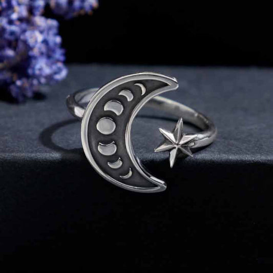 Close up of a shiny sterling silver adjustable ring for women.  One side has a larger crescent moon shape with inset moon phases and the other side has a shiny silver star with the band having an opening. 
