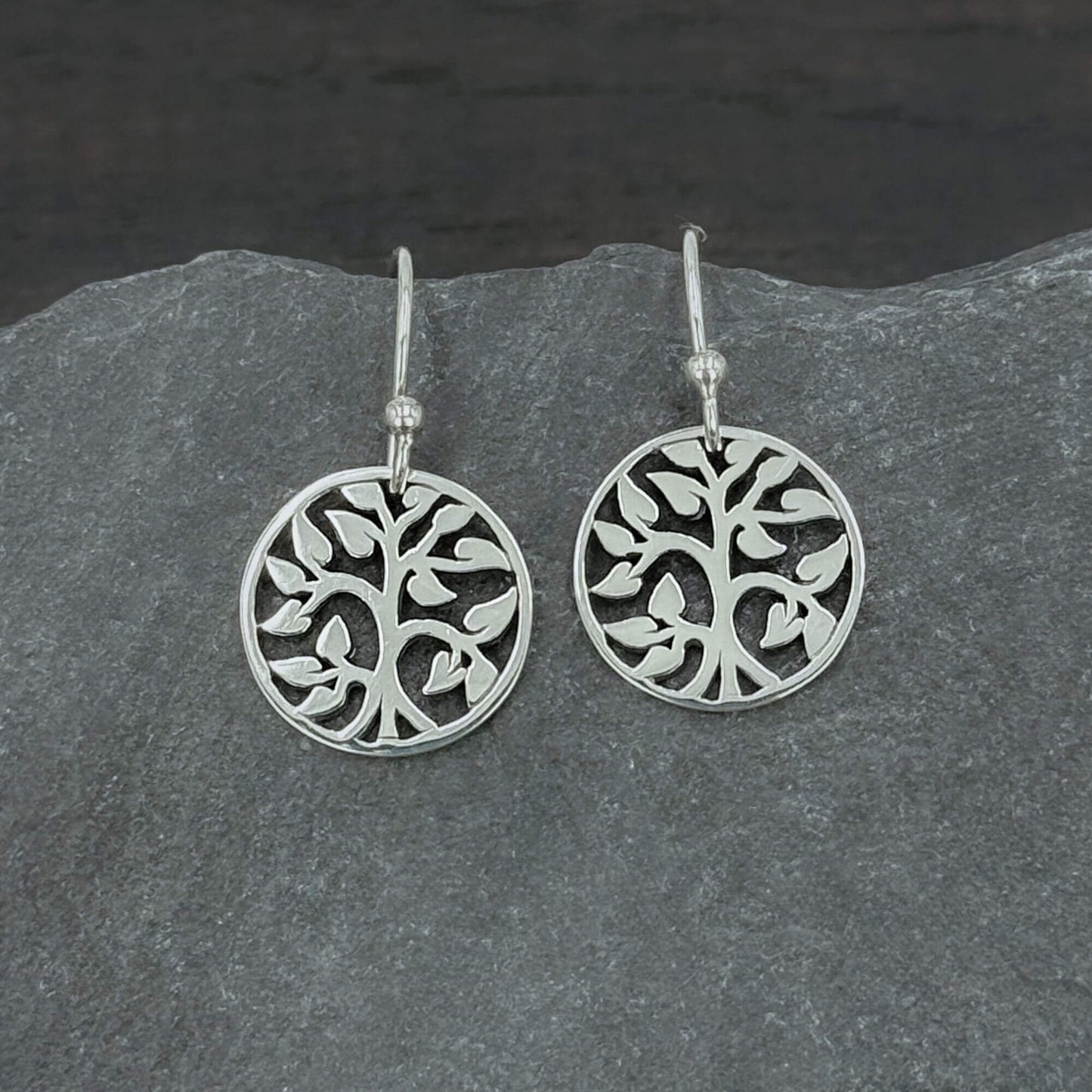 Close up view of 925 solid sterling silver earrings dangling from hook earwires with small circular Tree of Life charms with an openwork cut out design.  The tree charms are 5/8" tall and dangle freely.  A perfect jewelry gift for nature lovers.